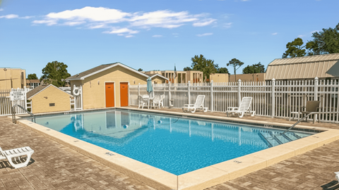 A pool with a brown building and white chairs.