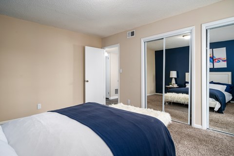 A bedroom with a bed and a mirrored closet door.