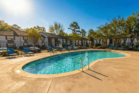 A sunny day at the pool with chairs and trees in the background.