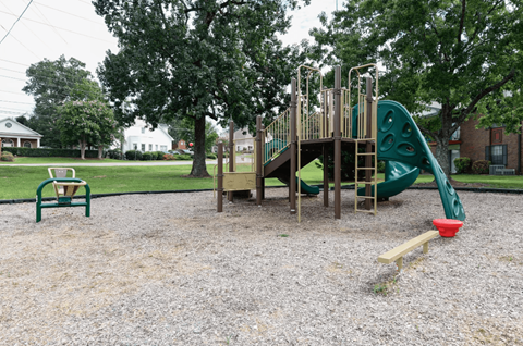 A playground with a green slide and a red bucket.