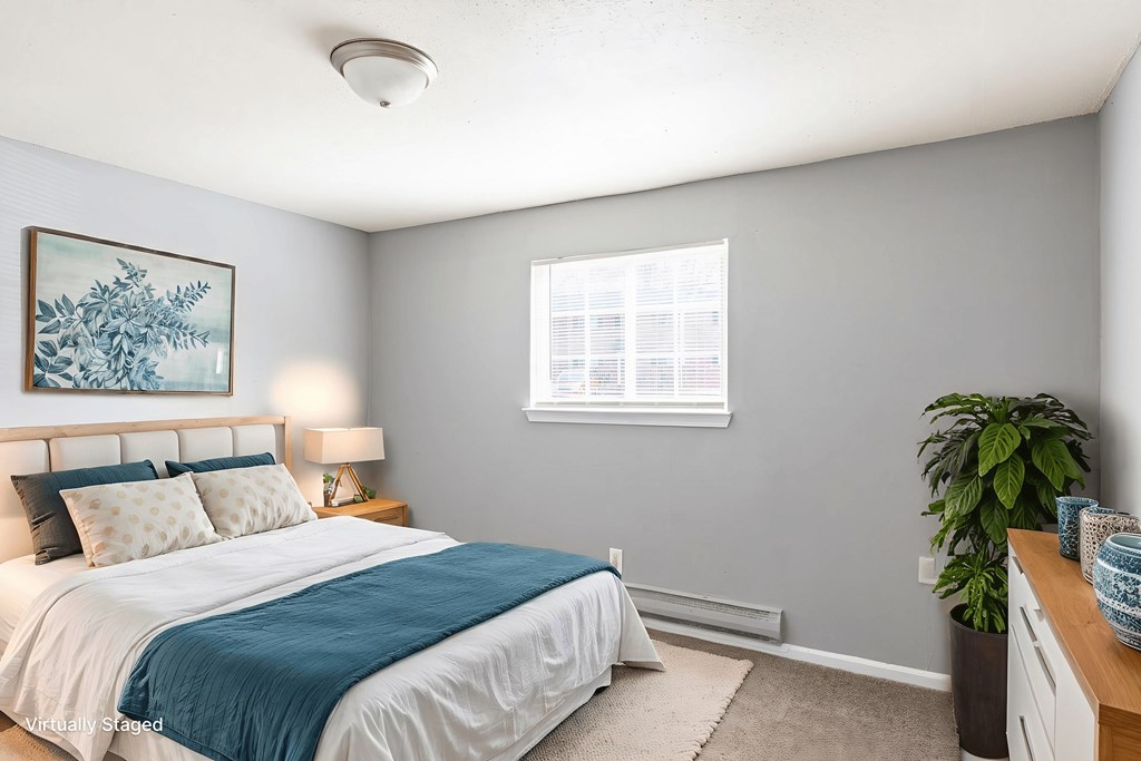 A bedroom with a bed, nightstand, and a plant.