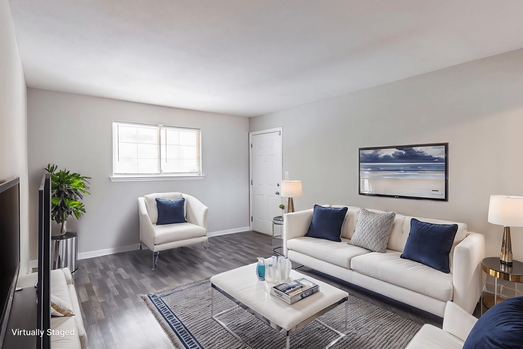 A living room with a white couch, a white chair, a coffee table, and a painting on the wall.