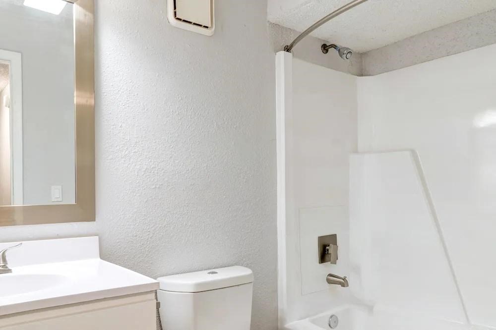 A white toilet is in a bathroom with a white sink and a white shower.