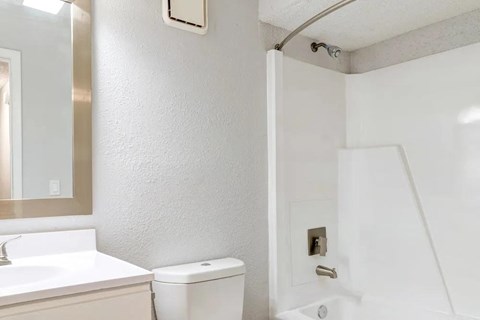 A white toilet is in a bathroom with a white sink and a white shower.