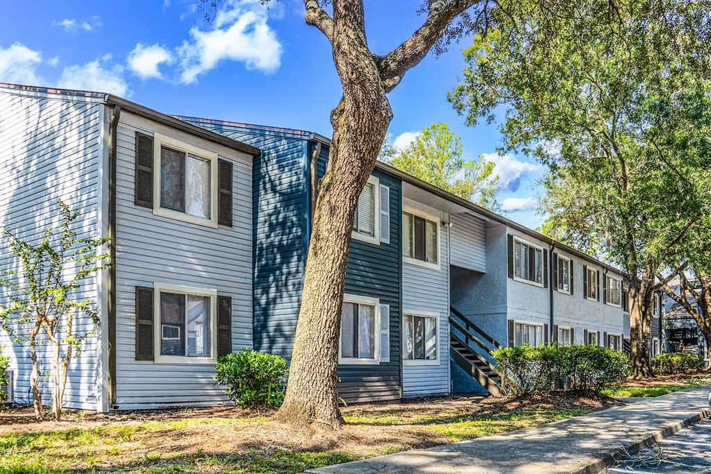 A tree stands in front of a two-story building with blue siding.