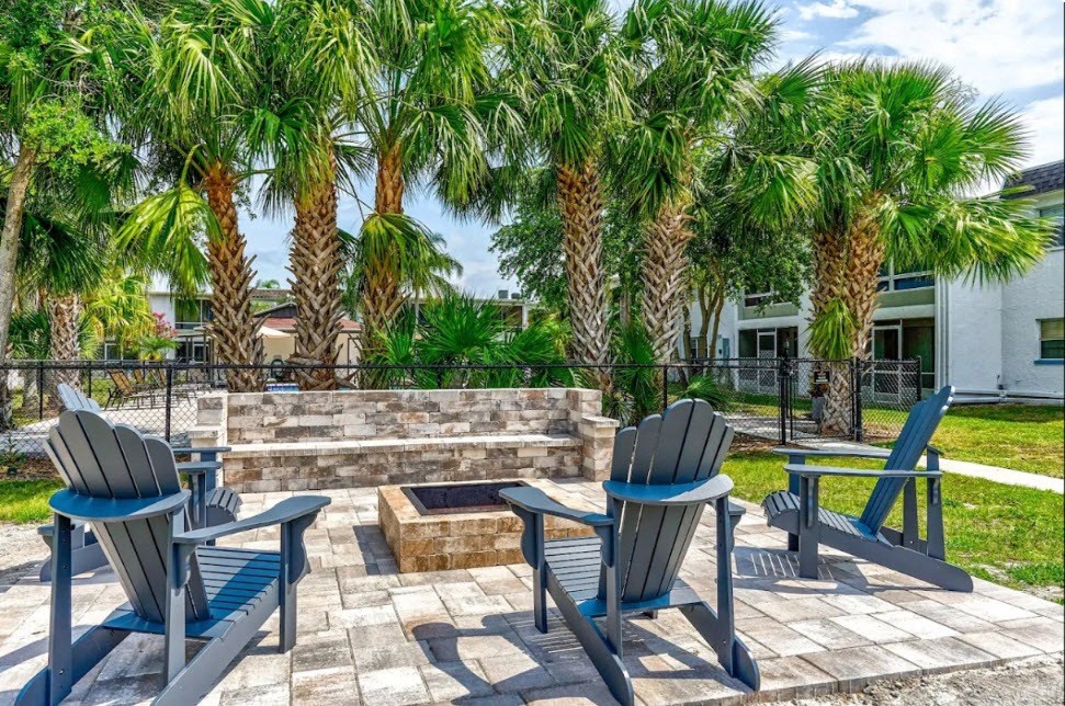 a patio with chairs and palm trees and a fire pit