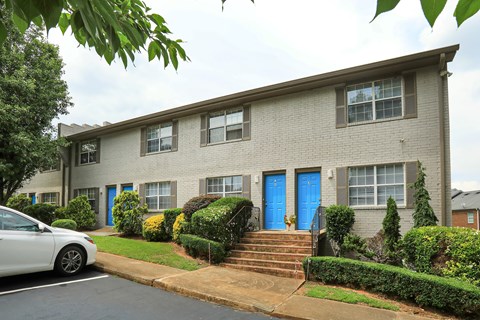A white car is parked in front of a grey building with blue doors.