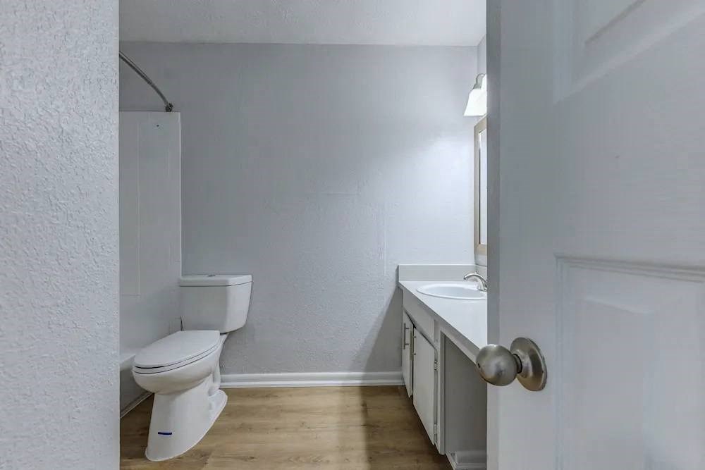 A white toilet is in a small bathroom with a sink and a door.