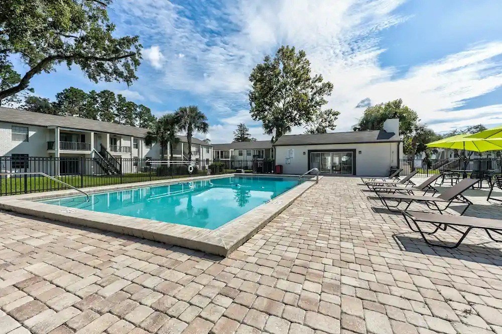 A swimming pool surrounded by a brick patio and lounge chairs.