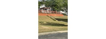 A red brick wall with a metal railing and steps leading up to a house.