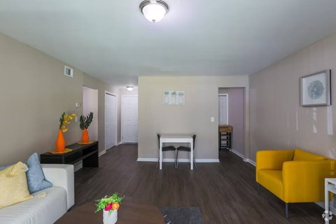 A living room with a white couch, a yellow chair, and a coffee table with a vase of flowers on it.