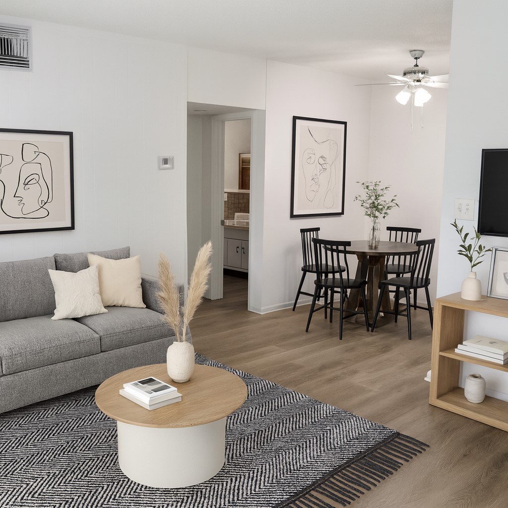 A living room with a grey sofa, a coffee table, a dining table with chairs, and a TV on the wall.
