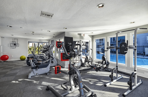 A well-equipped gym with a variety of exercise machines and a view of the pool outside.
