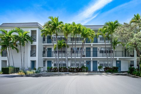 A large white building with balconies and palm trees in front.