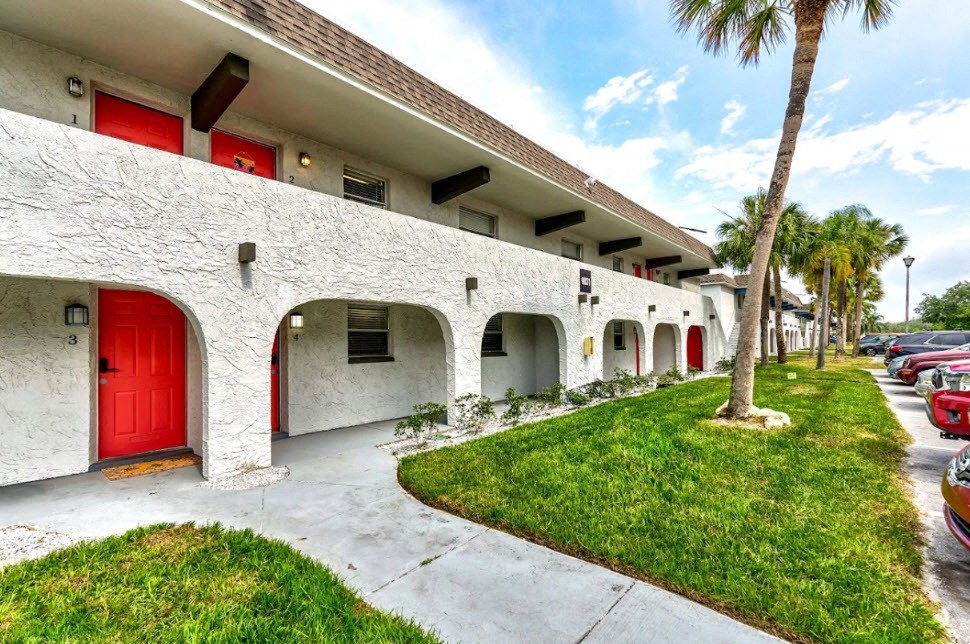 a white building with a red door and grass and palm trees