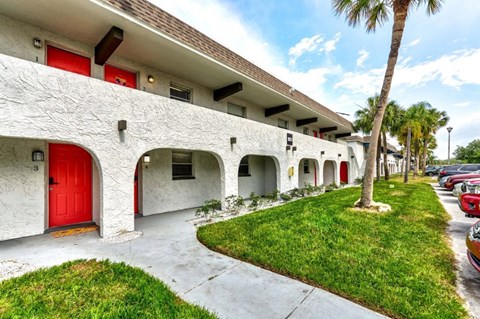 a white building with a red door and grass and palm trees