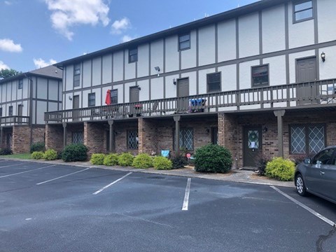A parking lot in front of a building with a flag on the balcony.
