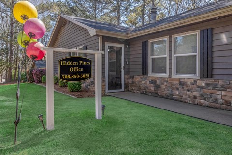 A sign for Hidden Pines Office with a phone number is in front of a house.