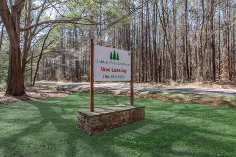 A sign in a grassy area that says "Hidden Pine Duplexes Now Leasing" with a phone number.