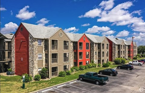 A row of red and beige buildings with cars parked in front.