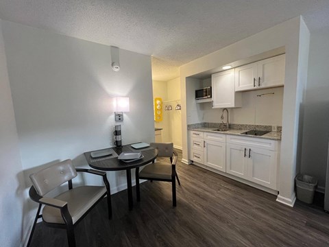 A kitchen with a table and chairs in the foreground and a countertop with a microwave and oven in the background.