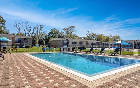 A swimming pool surrounded by a brick patio and lounge chairs.