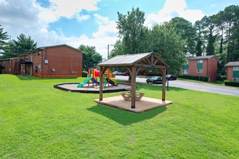 A playground with a swing set and a wooden pavilion is in the foreground of a grassy area.
