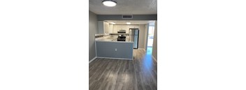 an empty living room with a kitchen in the background