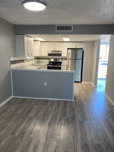 an empty living room with a kitchen in the background