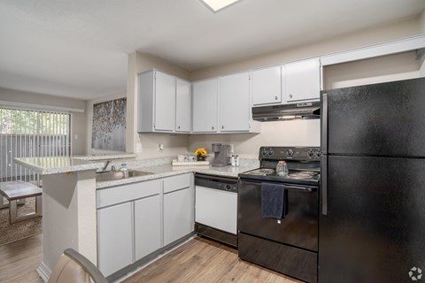 A black fridge sits in a kitchen with white cabinets and a black stove.