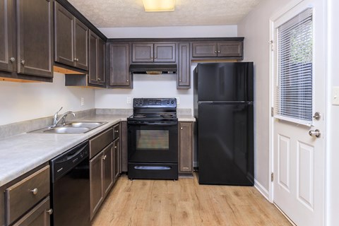 A black refrigerator sits in a kitchen with wooden floors and white walls.
