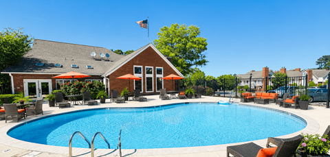 A pool with a red umbrella and a building in the background.