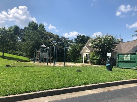 A playground with swings and a slide is located in a grassy area near a house.