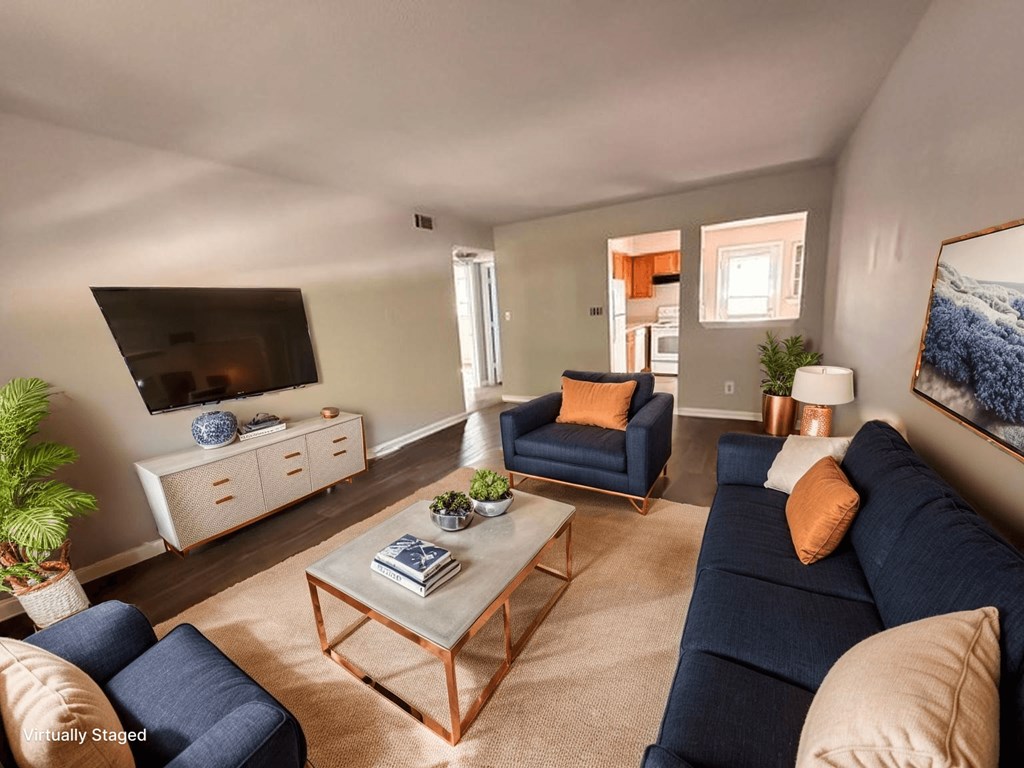 A living room with a blue couch, a white coffee table, and a TV on the wall.