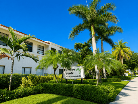 A sign for Camino Verde Senior Apartments is in front of a building with a palm tree.