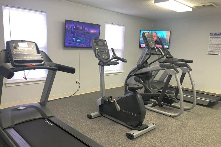 a gym with exercise equipment and televisions in a room