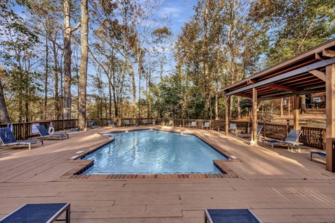 the pool is next to a deck with chairs and a pavilion
