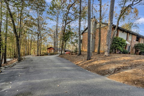 the driveway to the house is paved with asphalt and has trees