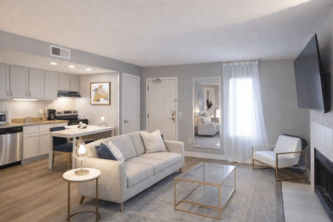 A living room with a white couch, a glass coffee table, and a flat screen TV mounted on the wall.