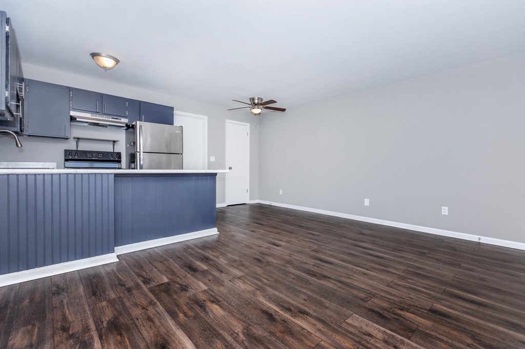 an empty living room with a kitchen and a ceiling fan