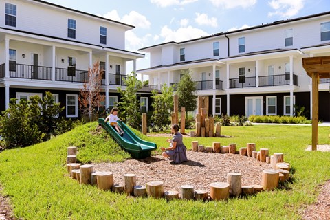 A child slides down a green slide in a playground.
