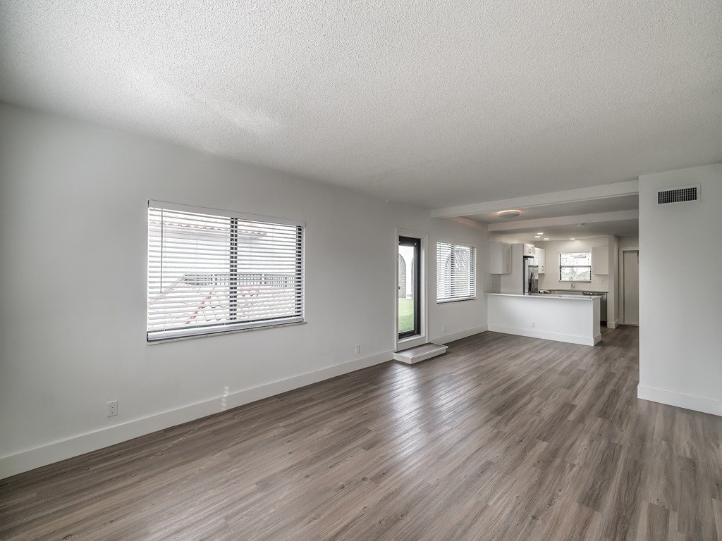 the living room and kitchen of an apartment with wood flooring and a window