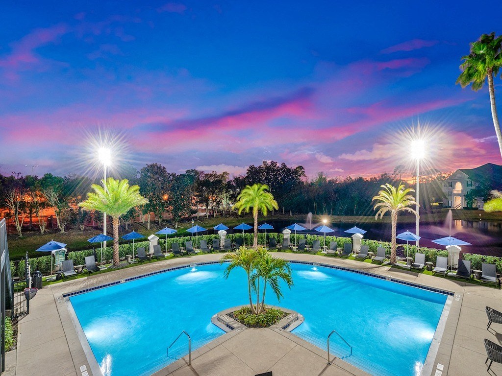 a swimming pool at night with palm trees and umbrellas