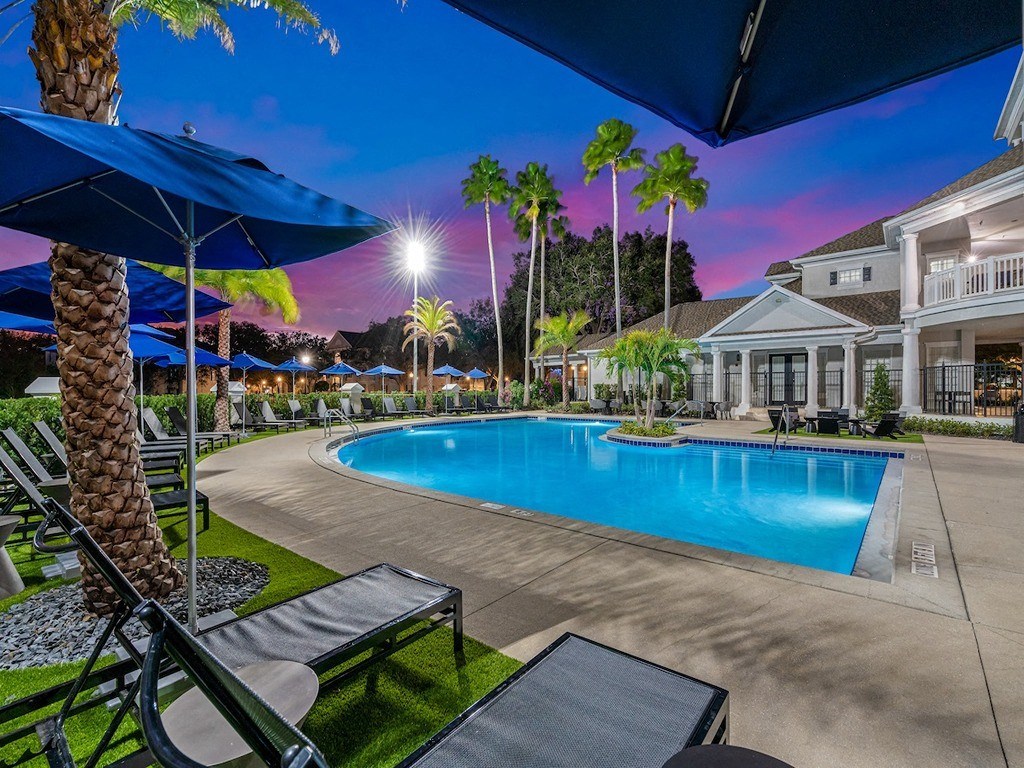 our resort style swimming pool is lit up at night with palm trees