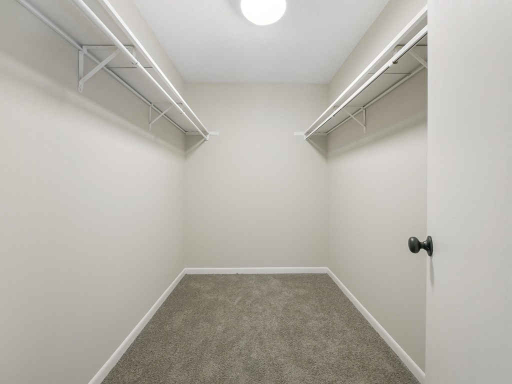 a room with a carpeted floor and white walls and a white closet with shelves