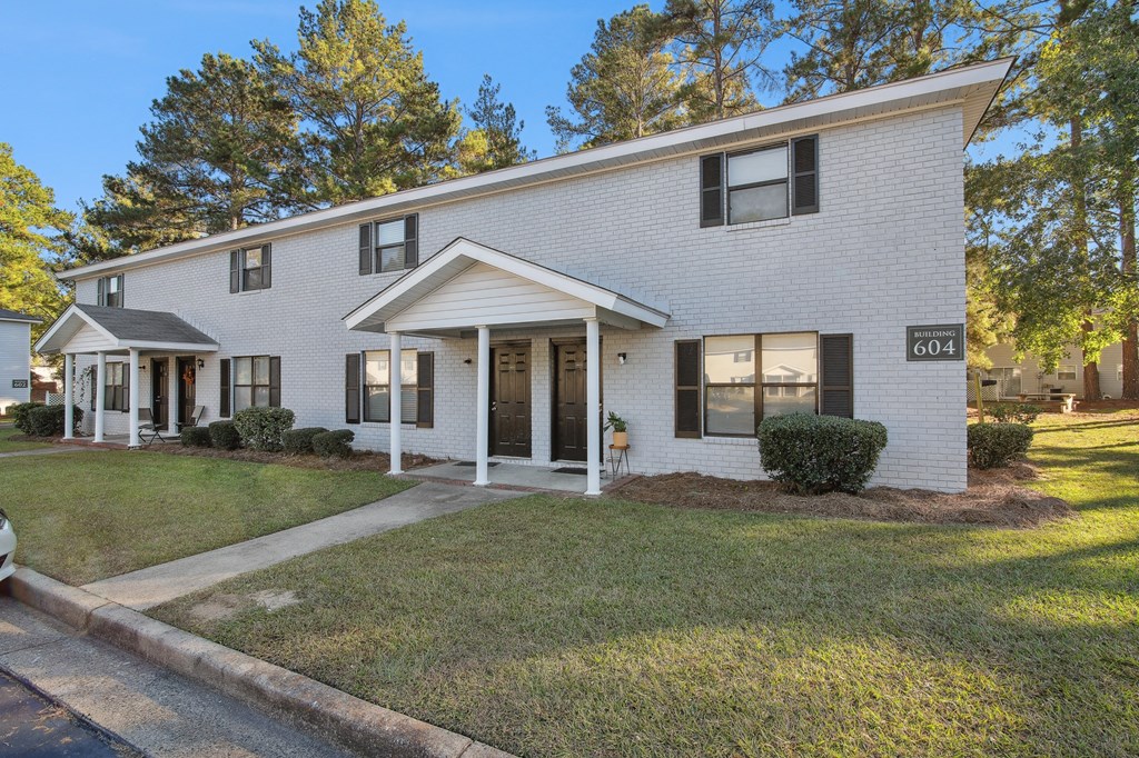 the front of a white house with a lawn and trees