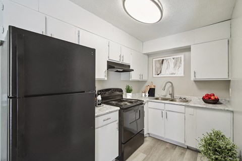 A black refrigerator stands in a kitchen with white cabinets and a black stove.