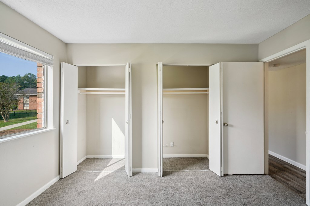 an empty bedroom with three closet doors and a window