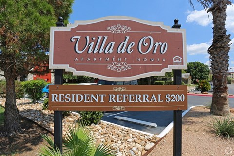 A sign for Villa de Oro Apartments and Homes with a resident referral offer.