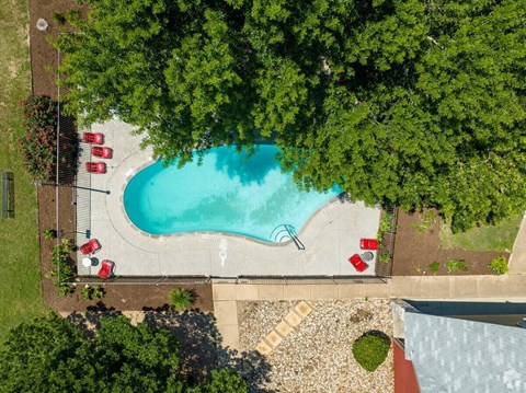 An aerial view of a swimming pool surrounded by trees and a parking area with red cars.